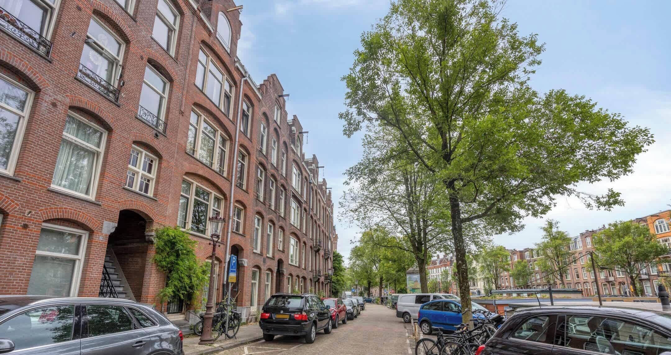 Eine Straße mit roten Backsteingebäuden, parkenden Autos und Fahrrädern.
