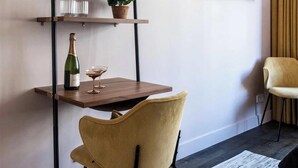 Een moderne woonkamer met een houten tv-meubel, een wandgemonteerde televisie, een eettafel met stoelen en een kamerplant.