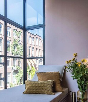 A window seat with cushions, a vase with yellow flowers, and a view of a building with multiple windows.