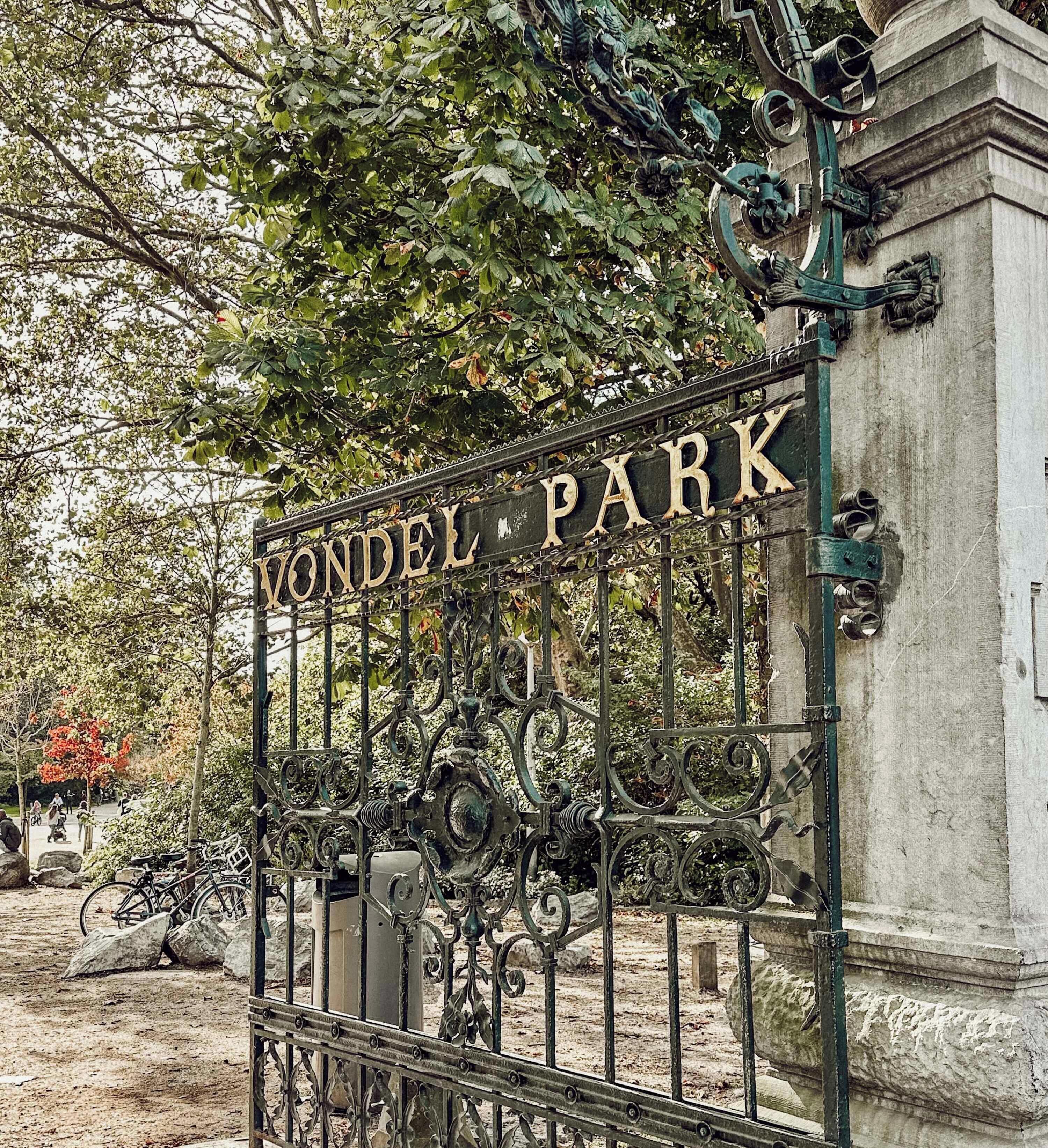 Een ijzeren poort met de tekst 'VONDEL PARK' in een park.