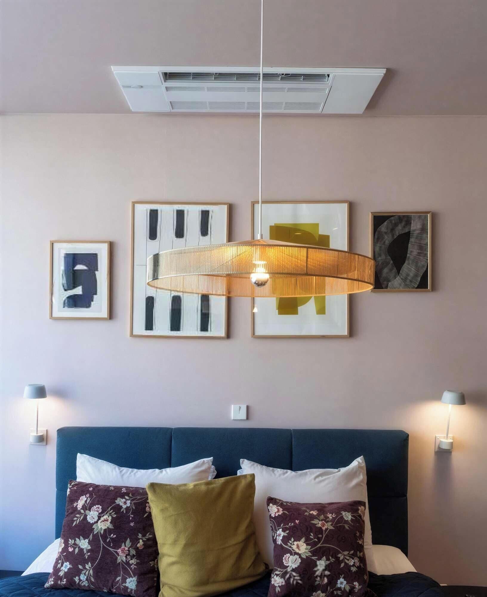 A bedroom with a blue sofa bed, floral pillows, a hanging light fixture, and wall-mounted lamps.