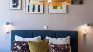A bedroom with a blue sofa bed, floral pillows, a hanging light fixture, and wall-mounted lamps.