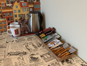 Et bord med en avis, en kaffekande, en kop og en æske med snacks.