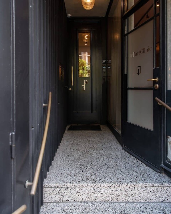 A hallway with a dark door, a glass door with a sign, and a staircase.