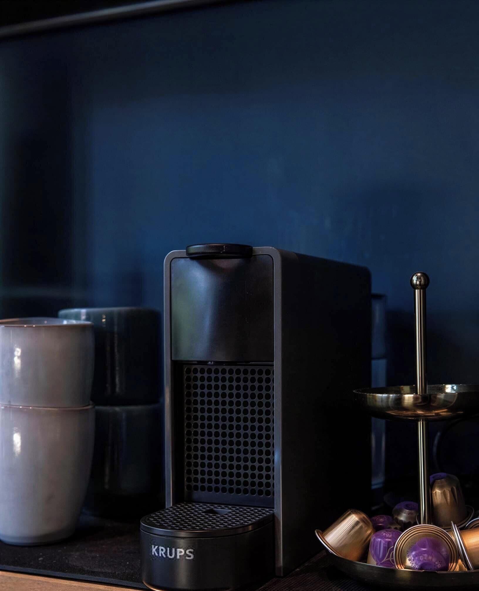 A black speaker, a KRUPS coffee grinder, and a candle holder with candles on a dark surface.