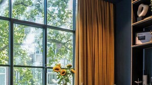 Een moderne kamer met grote ramen, een glazen tafel, twee stoelen, een boekenkast en een vaas met zonnebloemen.