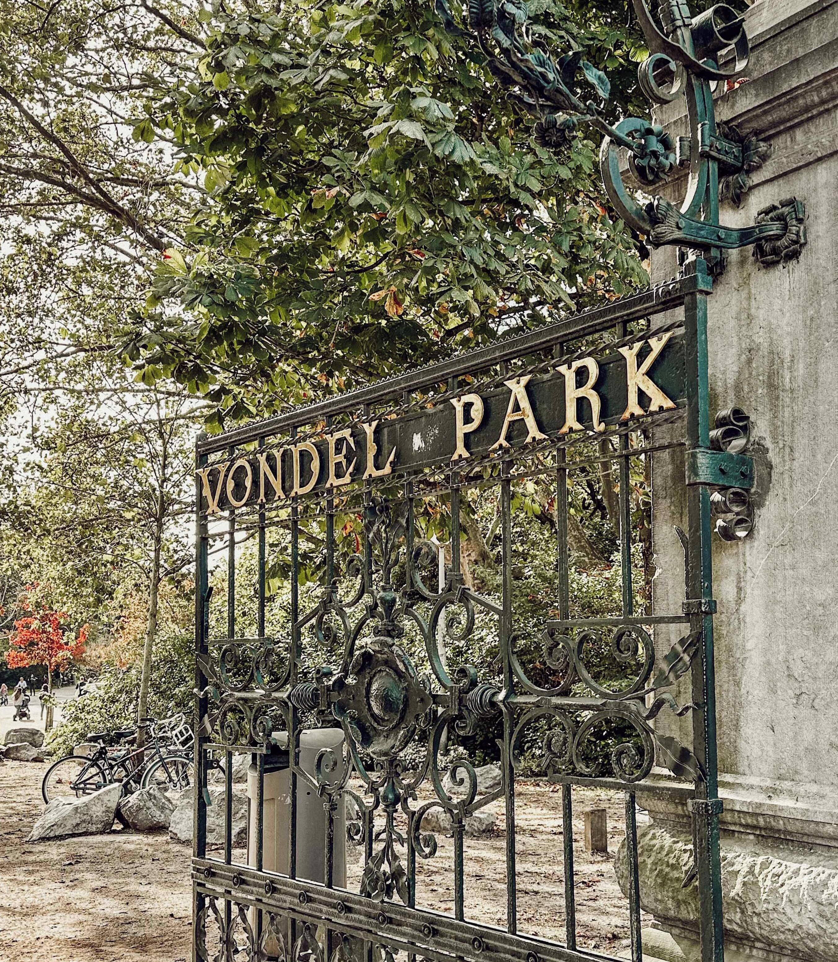 Een ijzeren poort met de tekst 'VONDEL PARK' in een park.