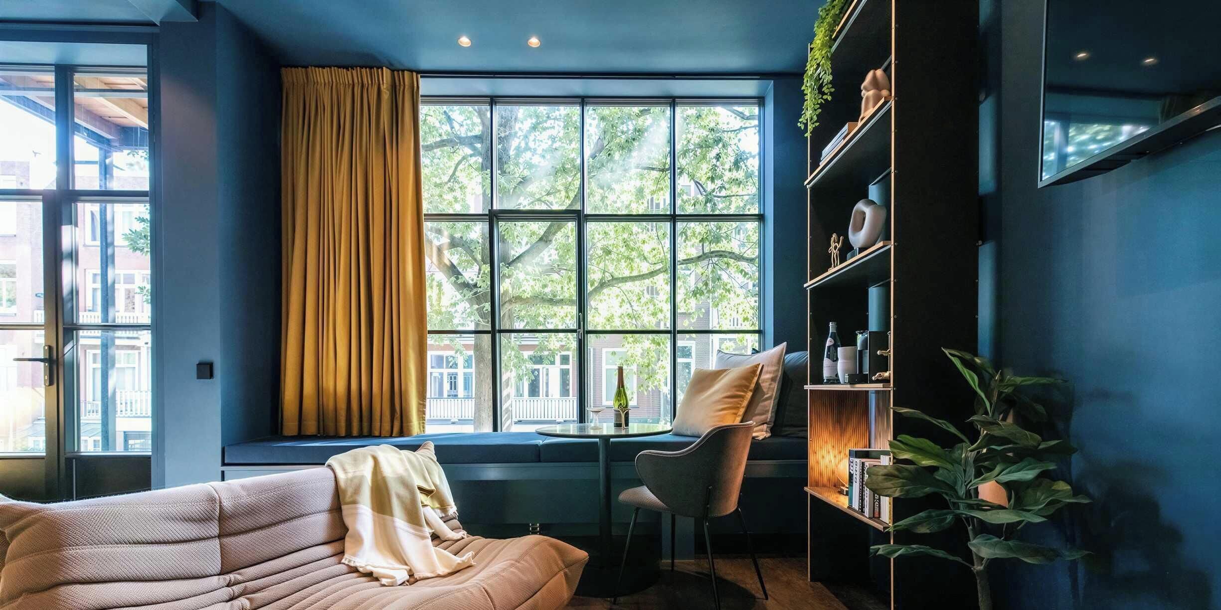 Een moderne kamer met een groot raam, een bank, een stoel en een boekenkast.
