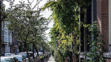 Een stoeprand met geparkeerde fietsen en bomen, met gebouwen aan één kant.