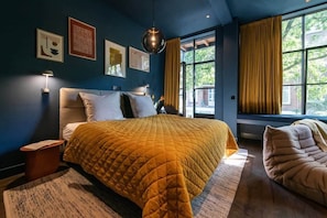 A bedroom with a large bed, a bedside table, a floor lamp, and a window with curtains.