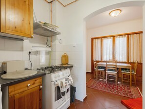A compact kitchen with a Bosch stove, wooden cabinets, a dining area with a table and chairs, and a red patterned rug. - Stefano by Interhome (Fonyód)