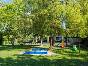 A playground with a blue sandbox, yellow and orange play structures, and green trees. - Stefano by Interhome (Fonyód)