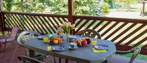 An outdoor patio with a table set for breakfast, including plates, cups, and a vase with flowers.