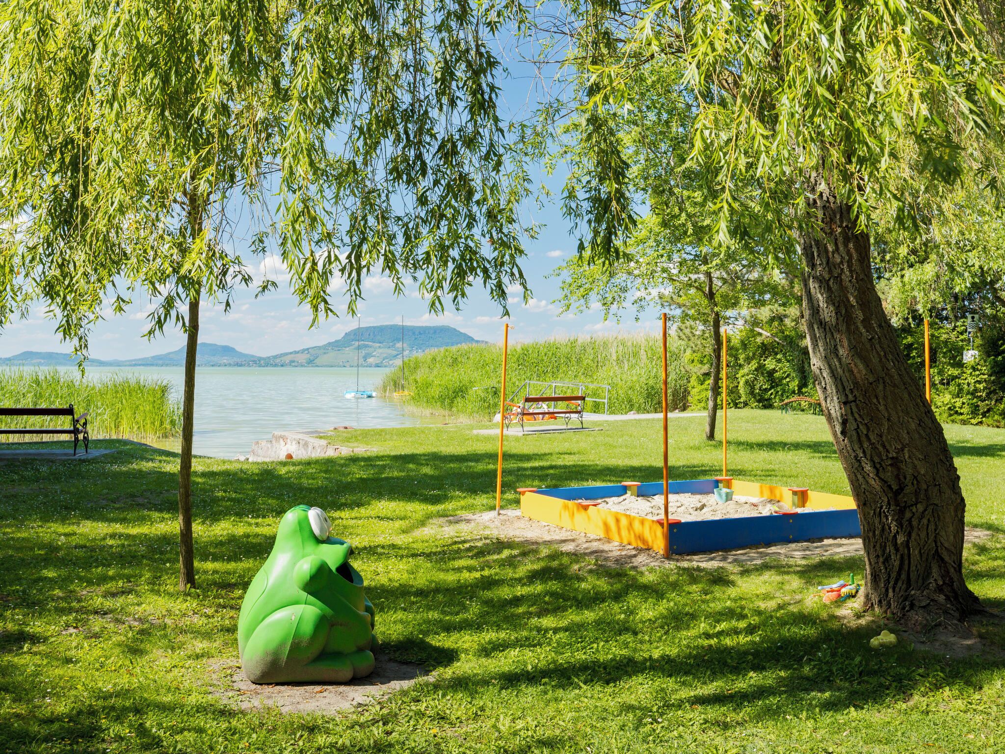 A park with a green frog sculpture, a playground, and a bench by a lake.