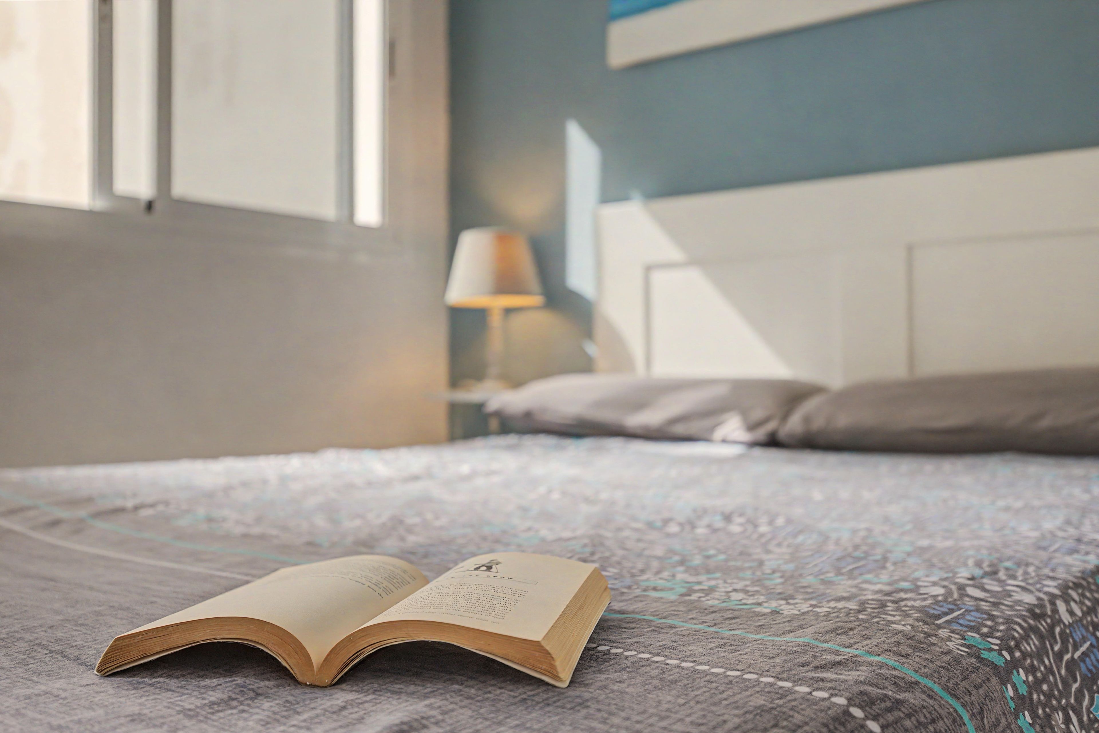Un lit avec un livre, une lampe et une fenêtre dans une pièce.