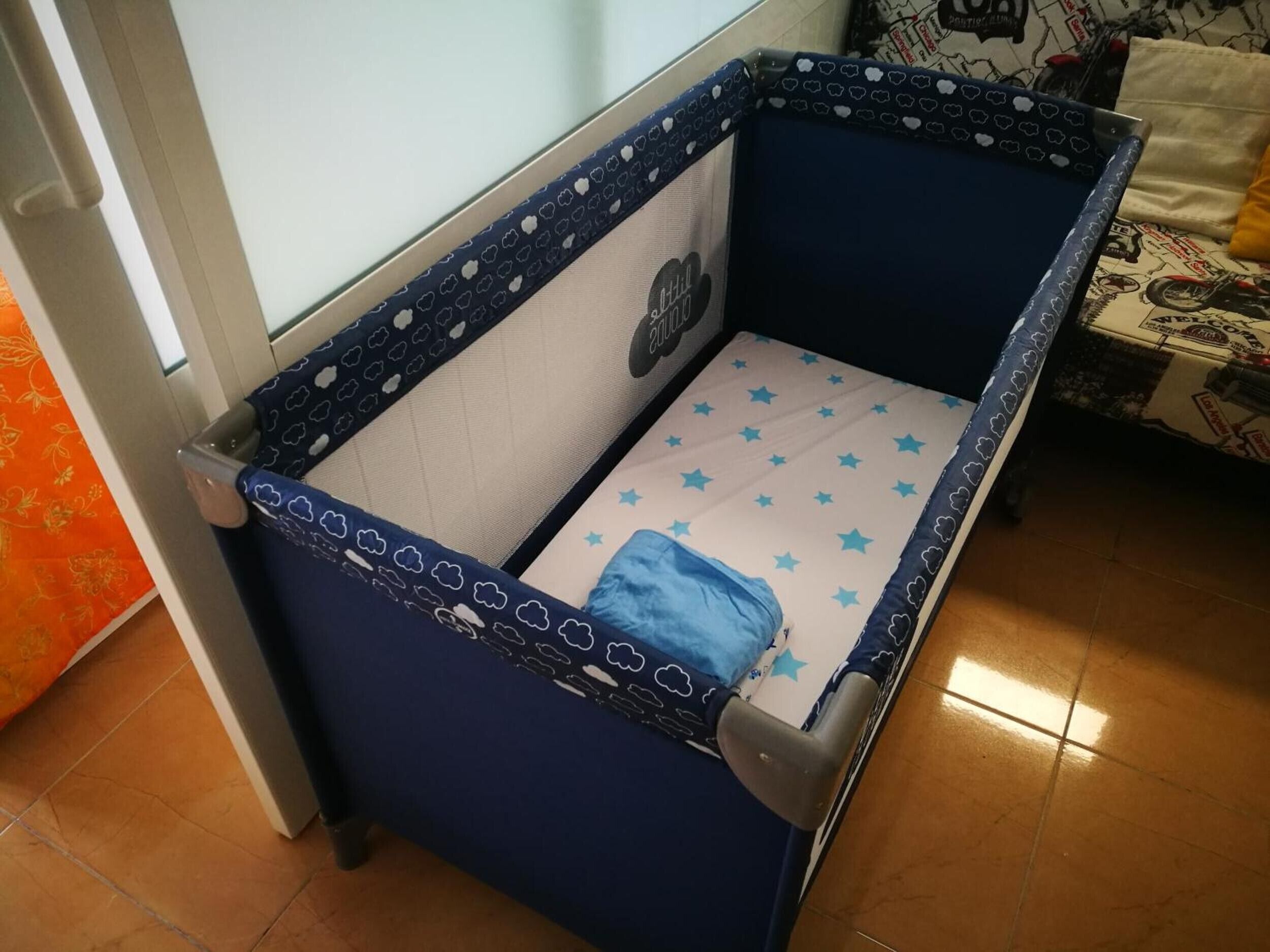 Una cuna con un colchón estampado de estrellas, un borde decorado con nubes y un pequeño peluche.