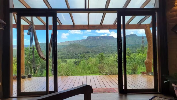 Une pièce dotée d’une grande porte-fenêtre coulissante qui donne sur une terrasse extérieure offrant une vue sur des collines verdoyantes et une chaîne de montagnes.