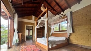 A room with a wooden four-poster bed, a patterned rug, and a view of greenery outside.