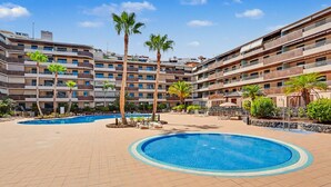 A hotel with multiple balconies, a swimming pool, and palm trees. - Vacation Apartment 'Balcón De Los Gigantes' with Sea View, Wi-Fi and Air Conditioning (Puerto de Santiago)