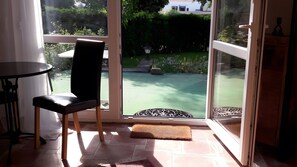 A room with a sliding glass door leading to a garden, a chair, a small table, and a mat at the door.