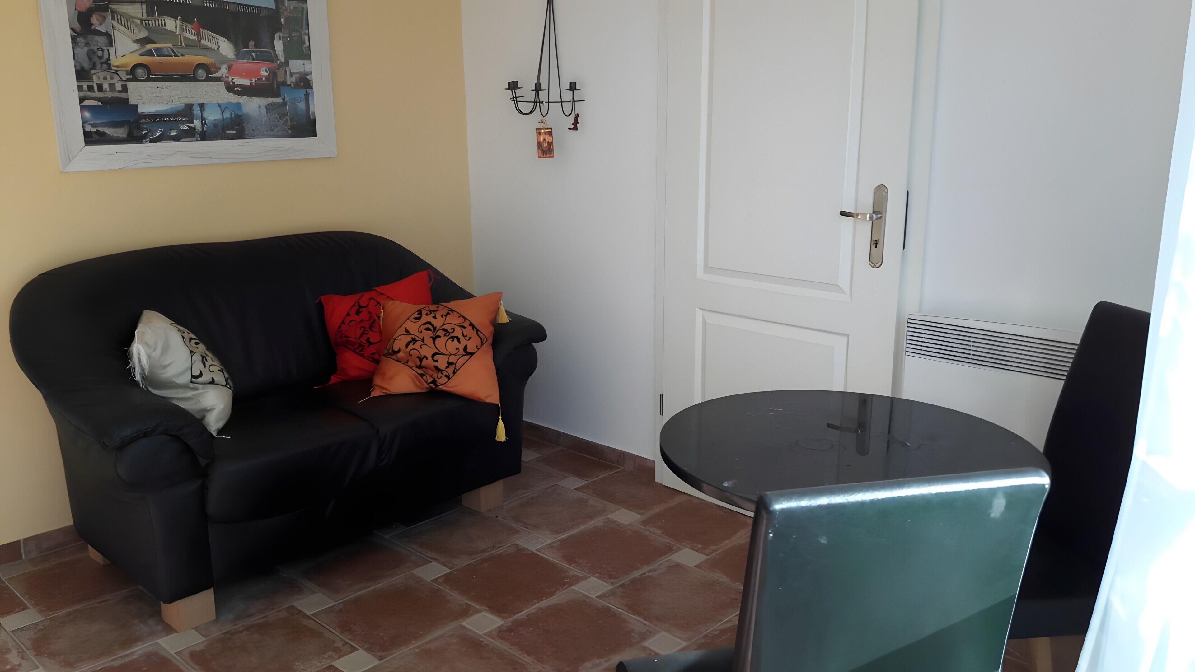 Ein Zimmer mit einer schwarzen Couch, einem kleinen Tisch, einer weißen Tür und einem Wandbild.