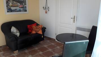 Ein Zimmer mit einer schwarzen Couch, einem kleinen Tisch, einer weißen Tür und einem Wandbild.