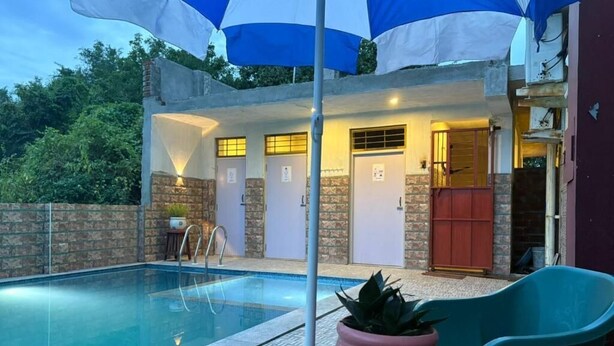 Una piscina con zona de patio, una planta en maceta y un edificio con puertas y ventanas.