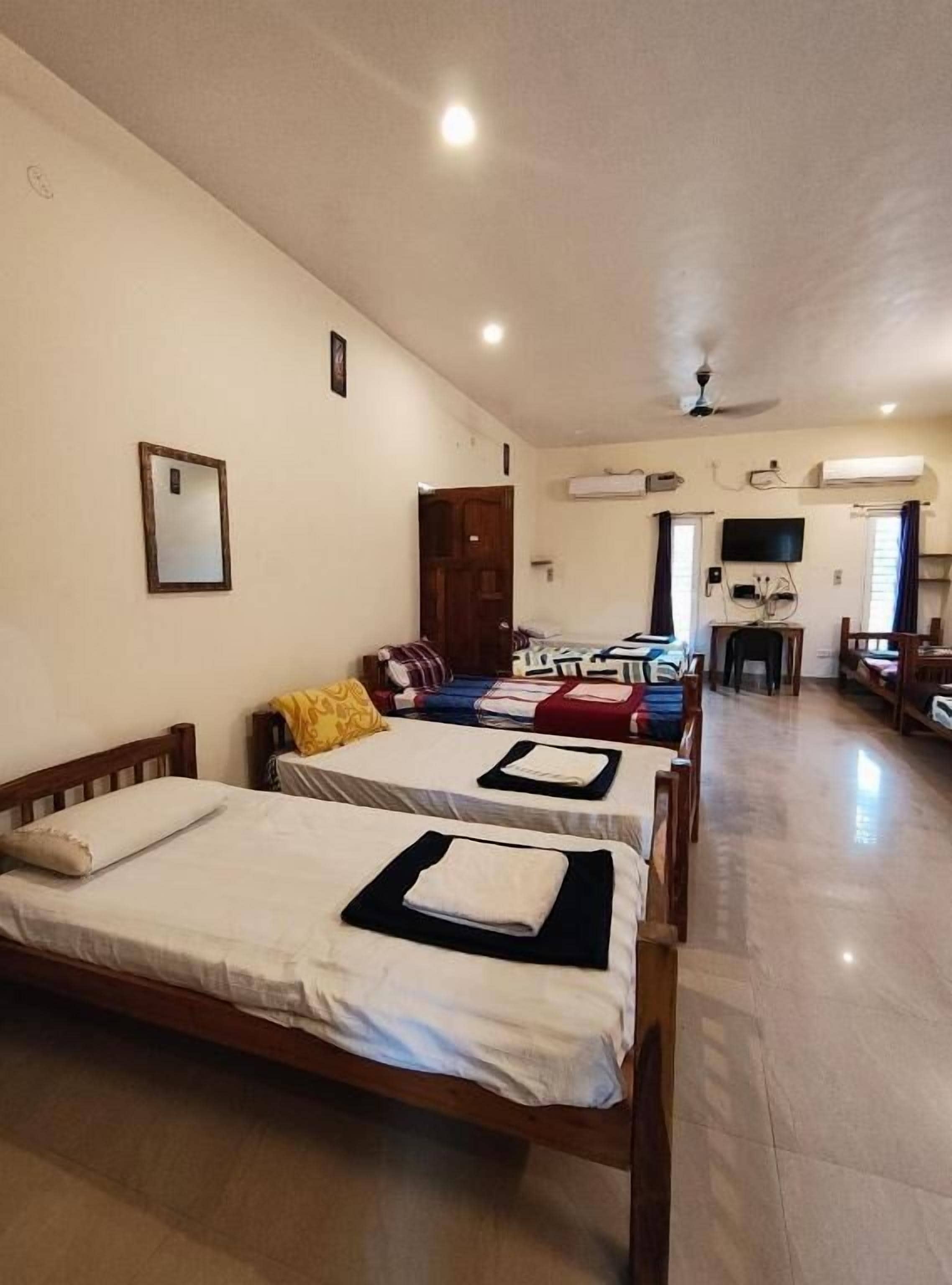 A hotel room with two wooden beds, a television, a ceiling fan, and a small table.