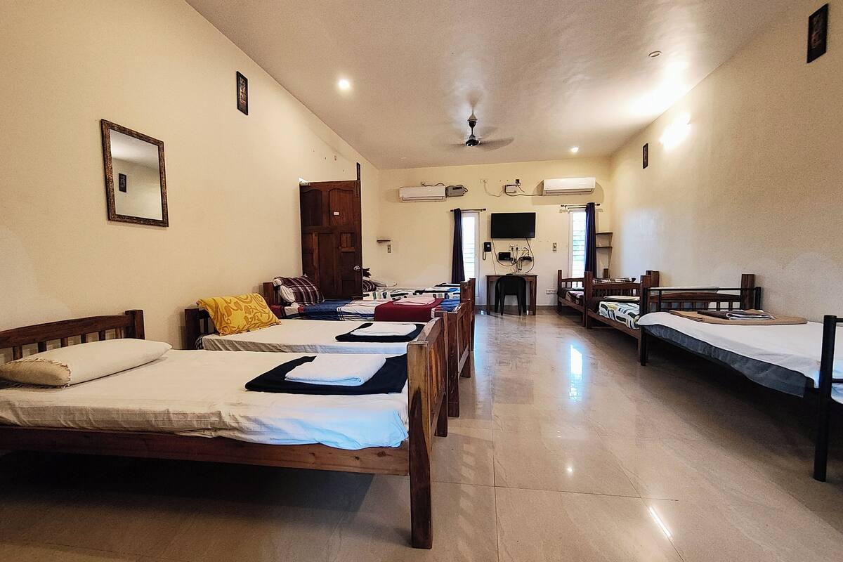 A hotel room with multiple beds, a ceiling fan, and a flat-screen TV mounted on the wall.