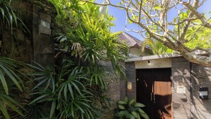 A traditional building with a wooden door, surrounded by lush greenery and a stone wall. - Sanga Villa by Betterplace (Pererenan)