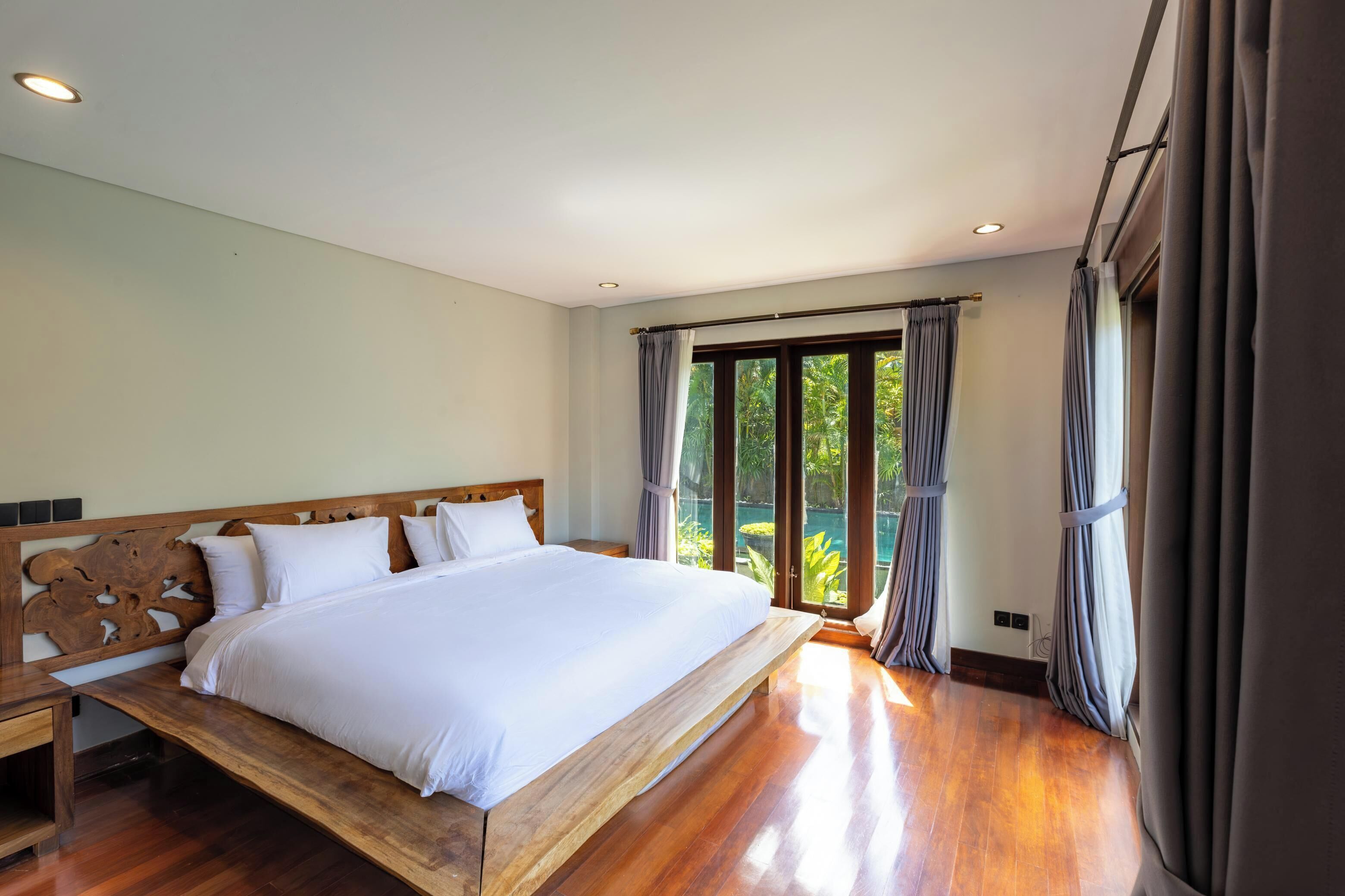 A bedroom with a large bed, wooden headboard, and a view through a glass door.