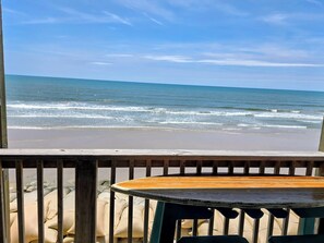 A wooden deck with a table and chairs, overlooking a beach with waves. - Oceanfront, Beachfront Condo 219 (North Topsail Beach)