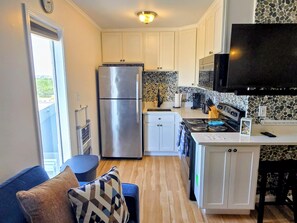 A compact kitchen with a refrigerator, stove, and microwave. There is a window with a view of greenery outside. - Oceanfront, Beachfront Condo 219 (North Topsail Beach)