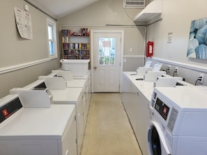 A laundry room with multiple washing machines, a bookshelf, and a door leading outside. - Oceanfront, Beachfront Condo 219 (North Topsail Beach)