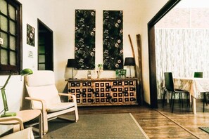 Ein Zimmer mit einem Sessel, einem kleinen Tisch, einem Schrank und zwei großen floralen Bildern an der Wand.
