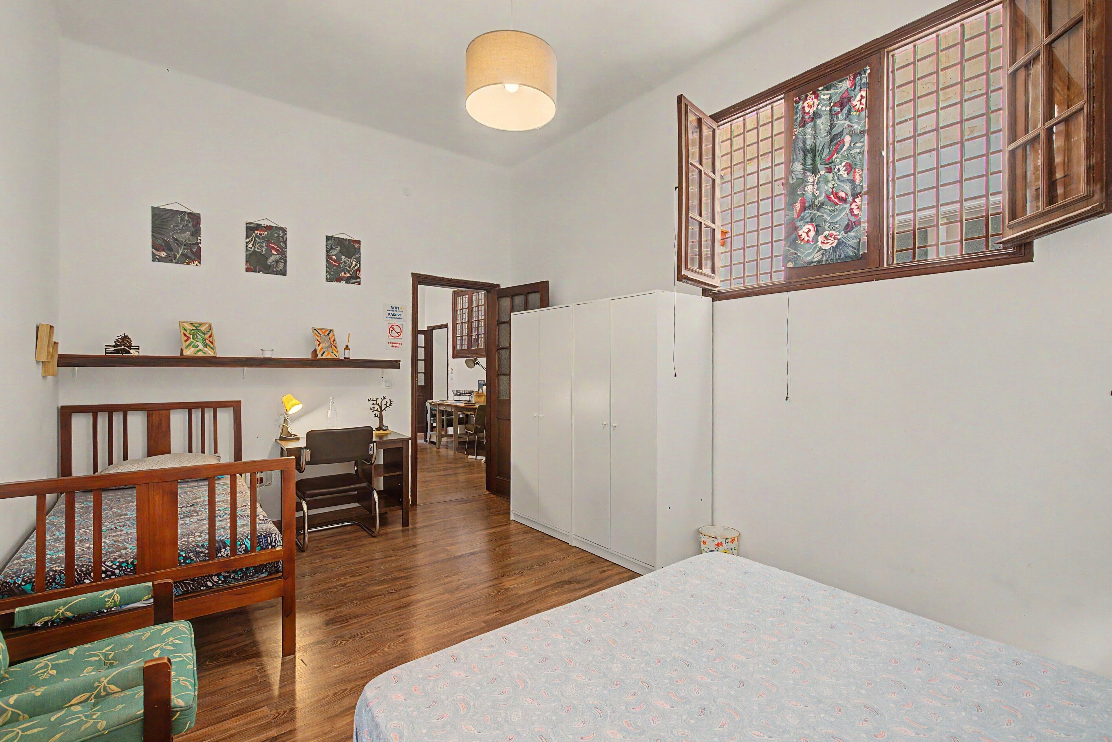 Una habitación con cama, escritorio, silla, armario y ventana con un panel decorativo.