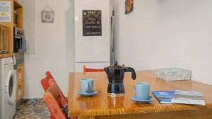 Een kleine keuken met een koffiezetapparaat, twee kopjes en een tafel met een tijdschrift.