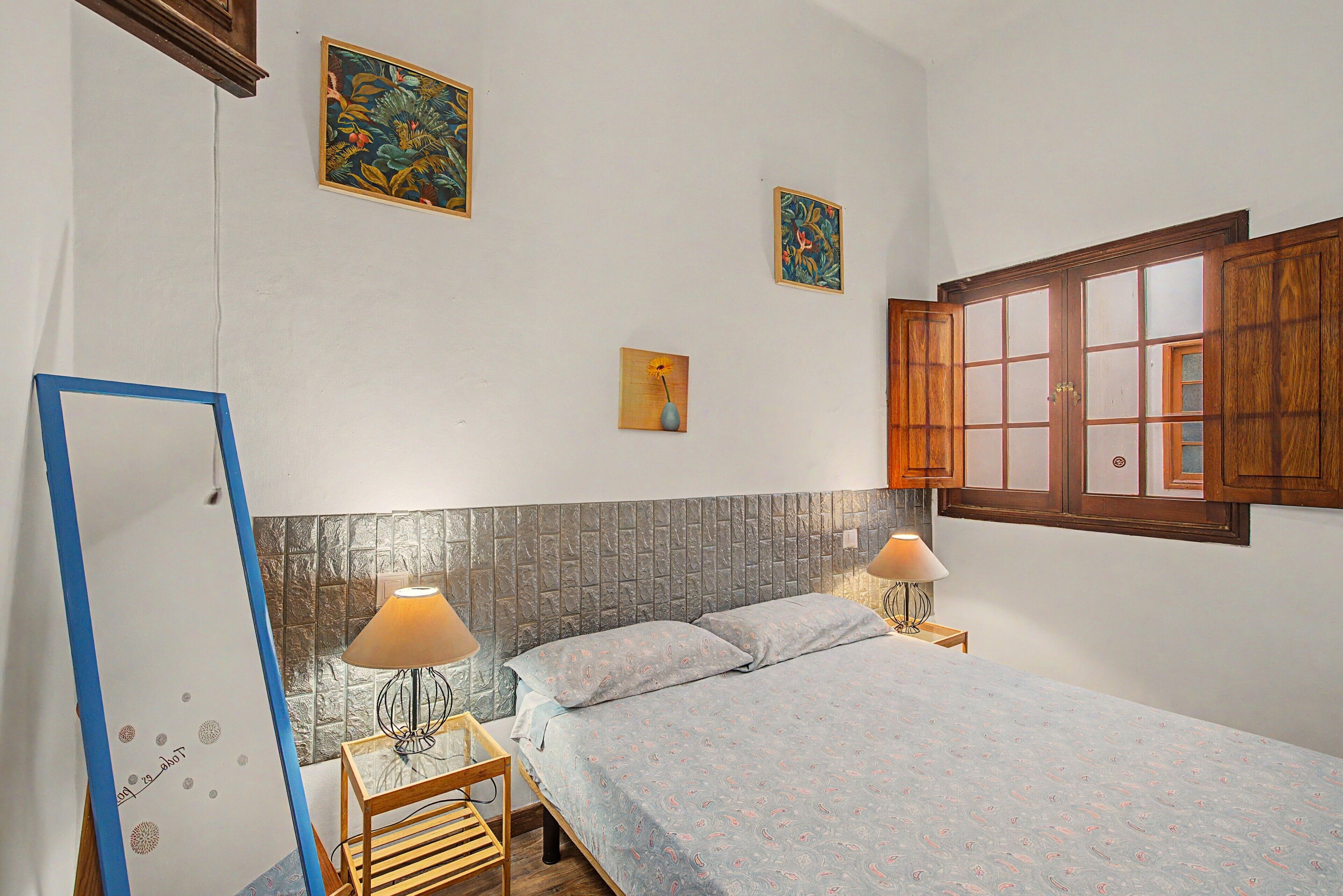 A bedroom with a bed, two bedside lamps, a wooden cabinet, and two wall-mounted paintings.