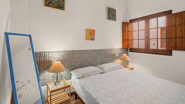 Een slaapkamer met een bed, twee bedlampen, een houten kast en twee wanddecoraties.