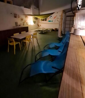 Ein Zimmer mit einem langen Holztisch, blauen Stühlen, einem weißen Tisch und gelben Stühlen.