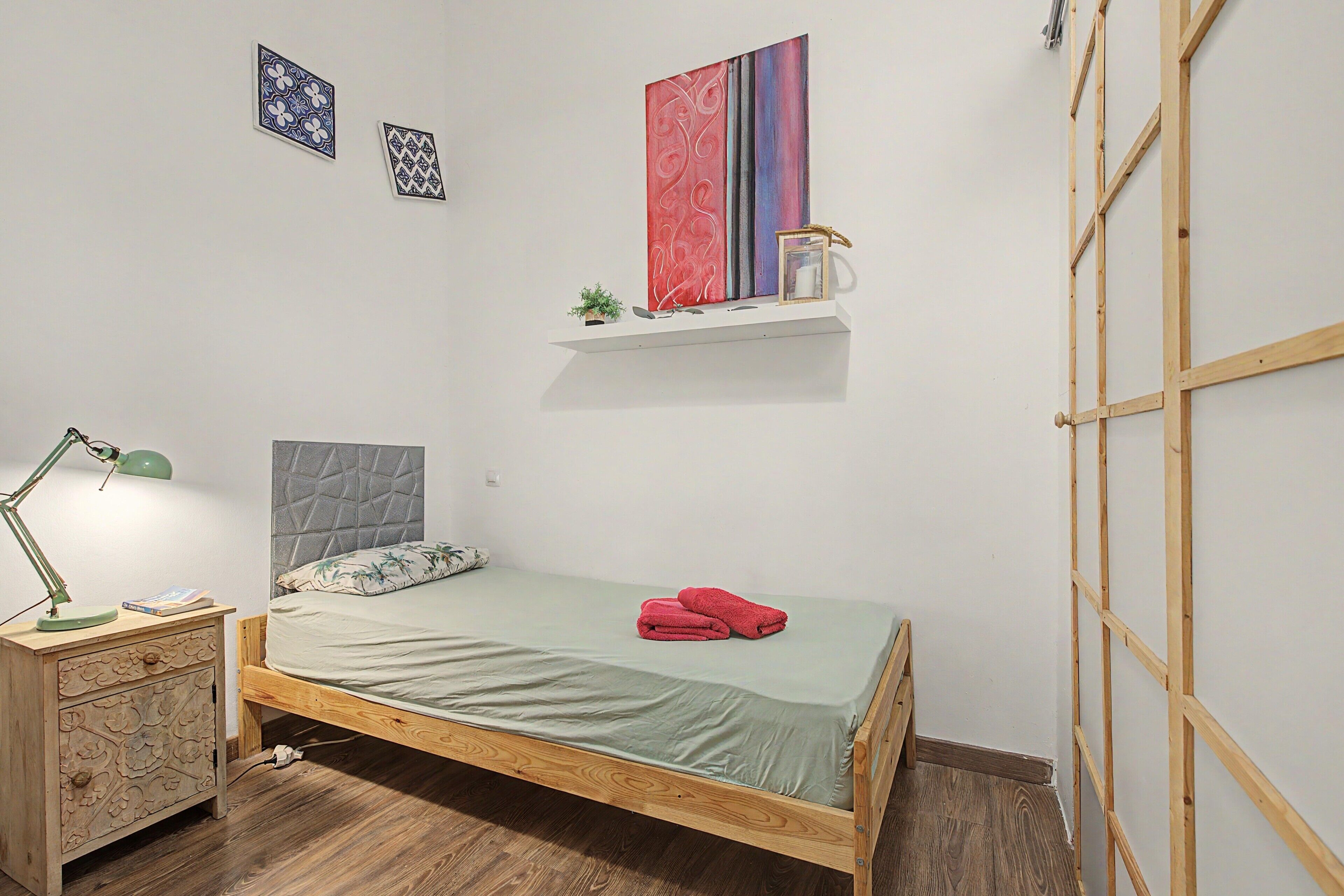 Un dormitorio con cama, mesita de noche, lámpara, estante con objetos decorativos y escalera de madera.