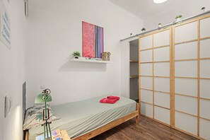 A small bedroom with a single bed, a shelf with decorative items, a wooden wardrobe, and a green floor lamp. - Single Room with Private Bathroom (Las Palmas de Gran Canaria)