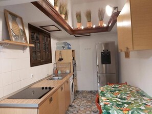 Eine kleine Küche mit Herd, Spüle und Kühlschrank, einer Waschmaschine und einem Bett mit blumigem Überwurf.