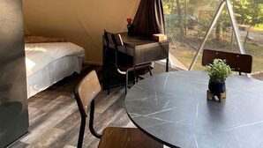 A tent with a bed, a table with chairs, and a view of trees through the window.