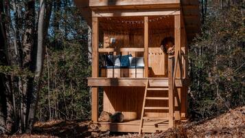 A wooden cabin with a lofted sleeping area, a ladder, and a small porch.