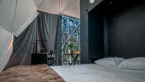 A bedroom with a bed, a desk, and a chair. There is a window with a view of trees.