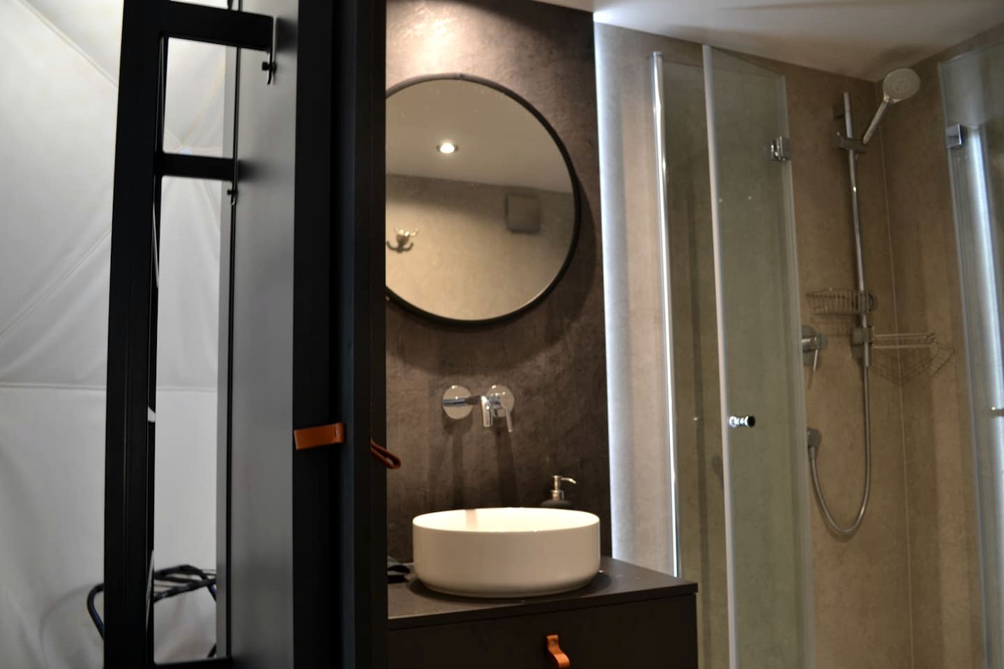 A modern bathroom with a round mirror, a sink, and a glass-enclosed shower.