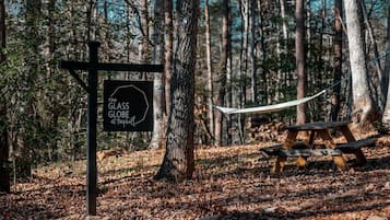 A hammock, a picnic table, and a sign in a forested area.