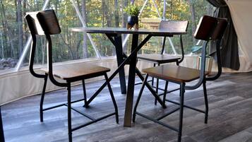 Una habitación con carpa, una mesa y cuatro sillas, ventanas amplias y vistas a árboles.