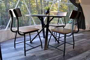 A tented room with a table and four chairs, large windows, and a view of trees.